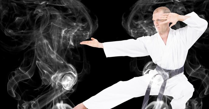 Composition of male martial artist over trails of smoke on black background