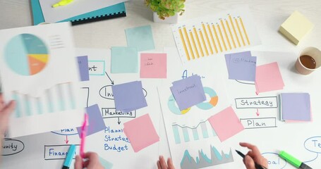 Business people discuss an idea in a meeting using financial charts and post stickers to plan a marketing strategy. Brainstorming team. Colleagues work on a project by analyzing statistics. 4K.