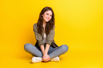 Photo of excited pretty young woman dressed brown shirt sitting floor empty space smiling isolated yellow color background