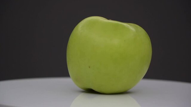 green and fresh apple spinning on white surface isolated on black