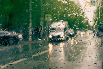 Car traffic through glass with raindrops. Sunny autumn day. Front view.