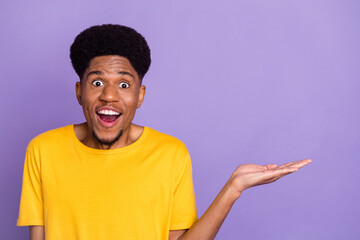 Portrait of attractive wondered cheerful guy holding on palm demonstrating copy space isolated over violet purple color background