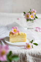 A piece of layered napoleon cake decorated with flowers on a light textile background, selective focus