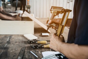 Carpenter using air nail gun doing wooden furniture work - obrazy, fototapety, plakaty