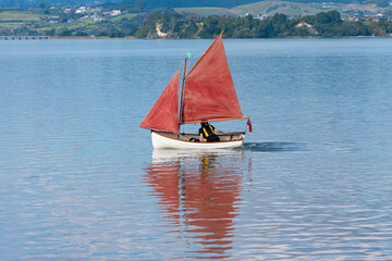 Traditional style red sails on small yacht becalmed in bay.