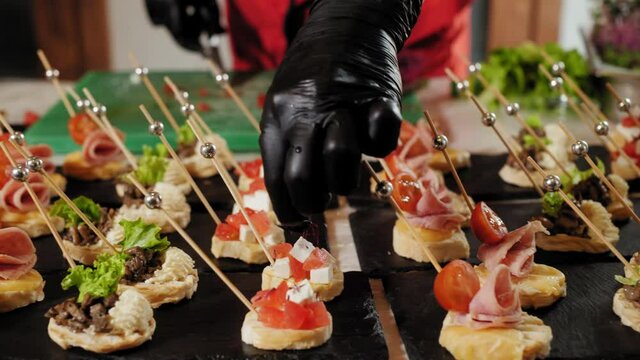 Close-up view of chef decorating gourmet canapes with microgreens. Cropped shot of hands in gloves preparing and serving delicious mini snacks