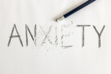 Erasing anxiety. Anxiety written on white paper with a pencil, partially erased with an eraser. Symbolic for overcoming anxiety or treating anxiety.   - obrazy, fototapety, plakaty