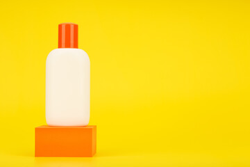 White cosmetic bottle with sunscreen lotion or cream with sunblock on orange podium against yellow background with copy space. Concept of safe tanning and summer skin care on vacation