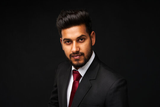 Portrait of young handsome indian business man in black suit on black isolated background