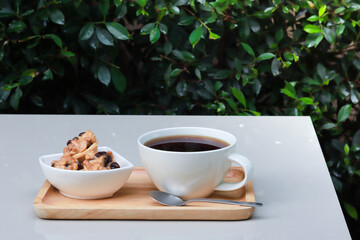 Coffee and cookie on wood tray on white table in the garden atmosphere, blurry green leaves...