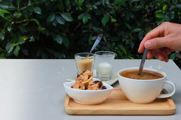 Coffee and cookie on white table in restaurant garden, green blurry leaves as back ground and a hand holding spoon to stir coffee.