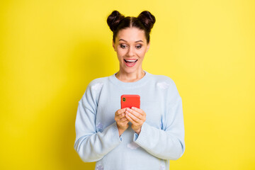 Portrait of attractive amazed cheerful girl using device chatting media news comment isolated over vibrant yellow color background