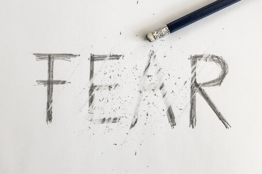 Erasing fear. Fear written on white paper with a pencil, erased with an eraser. Symbolic for overcoming fear or treating fear.