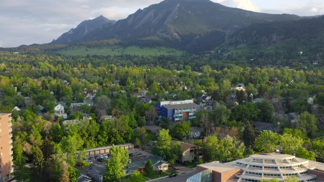 Aerial pan up reveal of beautiful flatiron mountain vista and bright green trees in Boulder Colorado during an evening sunset with warm light on the rocky mountain town and summer landscape