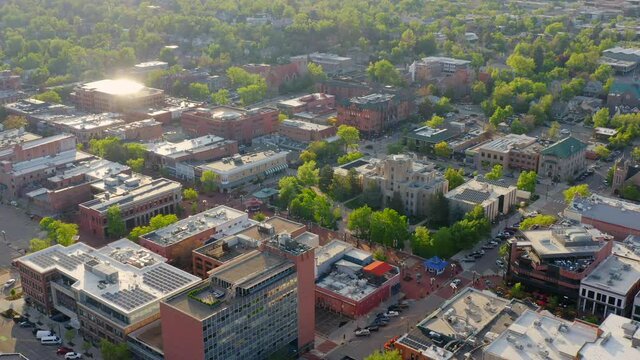 Aerial pan right of downtown Boulder Colorado and Pearl Street with bright green trees during an evening sunset with warm light on the summer landscape