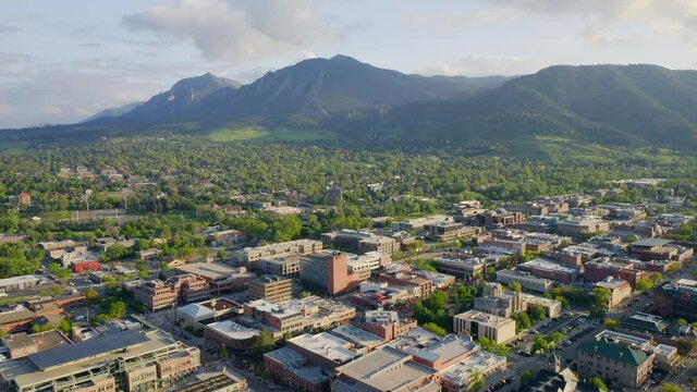 Aerial shot forward of beautiful flatiron mountain vista and bright green trees in downtown Boulder Colorado during an evening sunset with warm light on the rocky mountain town and summer landscape