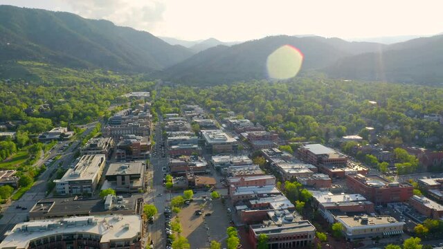 Aerial shot of beautiful mountain vista, bright green trees, and Pearl Street in downtown Boulder Colorado during an evening sunset with warm light on the rocky mountain town and summer landscape