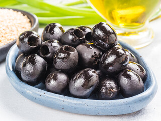 Close up view of black olives in blue plate on gray concrete background. Olive oil, green onion and quinoa in background
