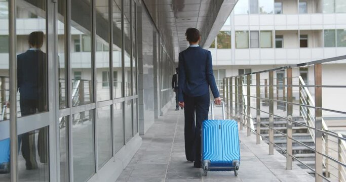 Back view of young attractive businesswoman walking with suitcase in airport