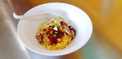 Grilled duck noodles and dumpling or dough with topping spring onion sliced and spoon on white bowl. Asian food in Hong Kong or Chinese style on stainless steel table at restaurant. 