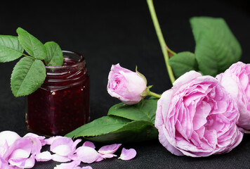 close up branch of tea rose with flowers jam and rose petals on black background