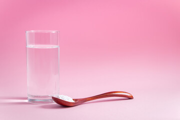 Natural bio supplement collagen powder in wooden spoon and glass of pure water on pink background....