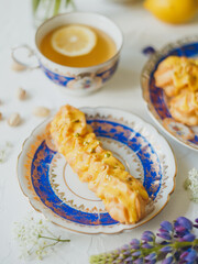 Lemon eclairs and lemon tea, in a vintage tea set, and flowers, over white background.