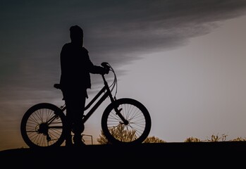 dziewczyna stojąca z rowerem na tle zachodu słońca - obrazy, fototapety, plakaty