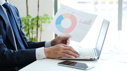 資料を片手にパソコンを操作するサラリーマン男性