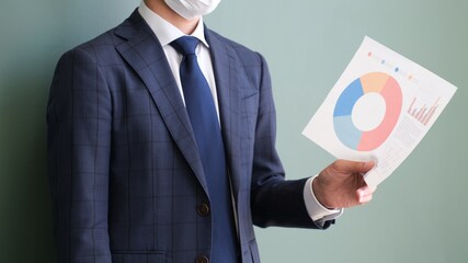 資料を持ちプレゼンをしているマスクをしたサラリーマン男性