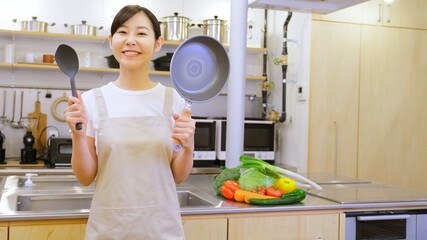 フライパンを持ちカメラ目線でほほ笑む家事代行の女性作業員