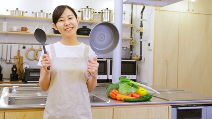 フライパンを持ちカメラ目線でほほ笑む家事代行の女性作業員