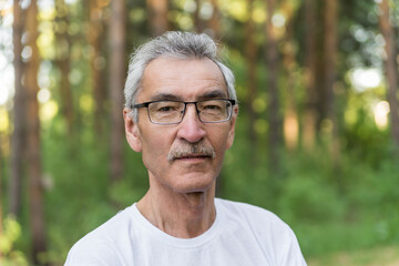 portrait of an elderly man on the background of the forest park. an old man of 60s against the...