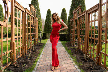Gorgeous woman in elegance red long  silk dress posing in summer  park.  Perfect wavy hairs. Full...