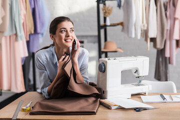 Seamstress talking on smartphone near cloth, ruler and sewing machine