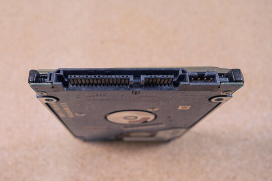 Close-up: a laptop hard drive stands on a surface with a sandy texture. Macro photo of the SATA connector and the power connector.