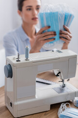 Sewing machine near blurred seamstress holding medical masks