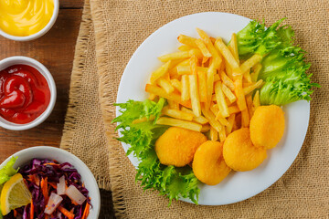 French fries with chicken nuggets near sauces on a napkin on a wooden table.