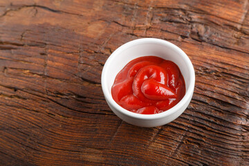 White gravy boat with ketchup on a wooden table.