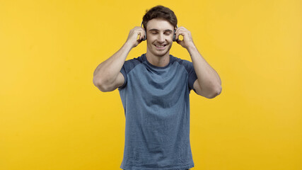 Smiling man listening music in headphones isolated on yellow