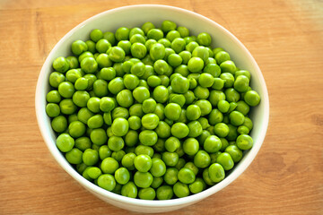 Green peas in white bowl with wooden background
