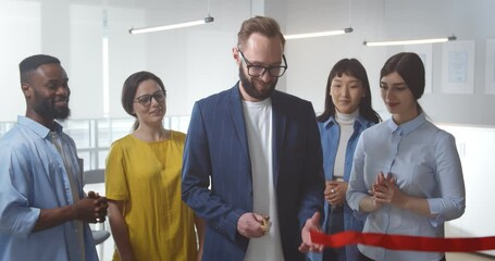 Portrait of smiling diverse young businesspeople cutting red ribbon in new office