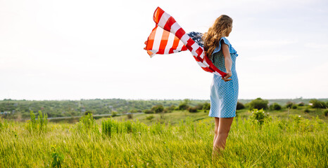 Happy woman posing with USA national flag standing outdoors in blooming meadow. 4th of July....