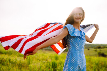 Happy woman posing with USA national flag standing outdoors in blooming meadow. 4th of July....