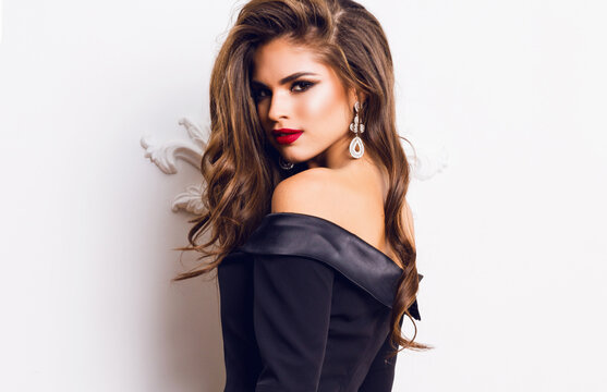  Beautiful stunning  woman with red full lips, smokey eyes make up , shining perfect  wavy hairs in  elegant casual black dress   posing on white background.