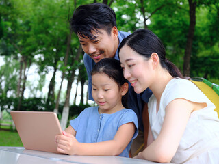 Happy family of three uses tablet computer outdoors