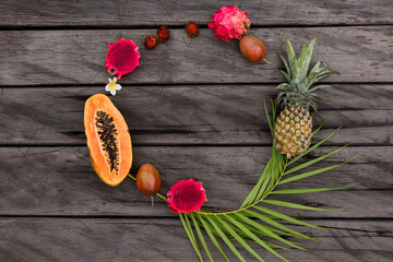 Obraz na płótnie Canvas Creative round composition with tropical fruits on wood background, top view. Slices of papaya, dragon fruit and pineapple. Palm leave. Copy space, top view.