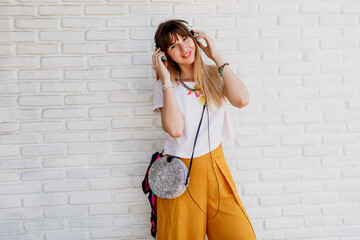 Smiling  woman posing over white brick wall with earphones and showing signs. Summer style. Positive mood.  Yellow sunglasses.