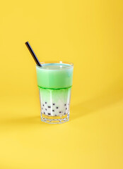 a glass of matcha latte tea with tapioca balls on a yellow background