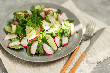 Cucumber, radish and spinach salad on a gray plate with a linen napkin on a gray background foreground in focus background in blur
